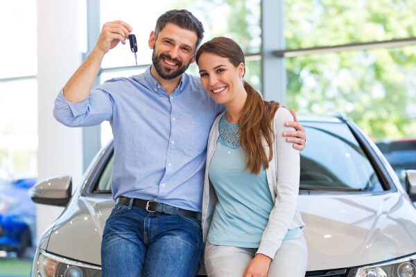 Casal feliz em frente a um carro novo segurando chave, simbolizando conquista através de empréstimo consignado Bevali.